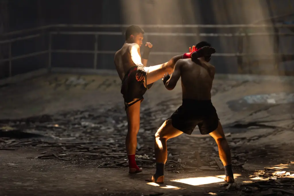 Two Muay Thai fighters exchanging strikes during a training bout under shafts of light
