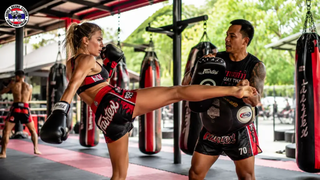 Woman practicing Muay Thai kicks with a trainer at a fight club in Phuket