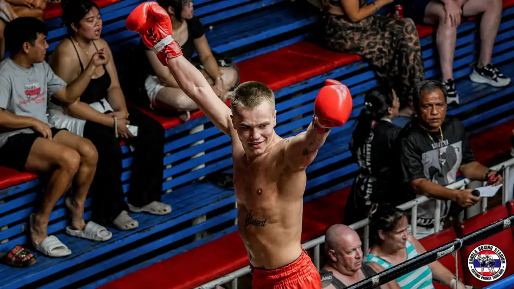 A victorious fighter celebrates his win with raised arms at a Phuket boxing stadium