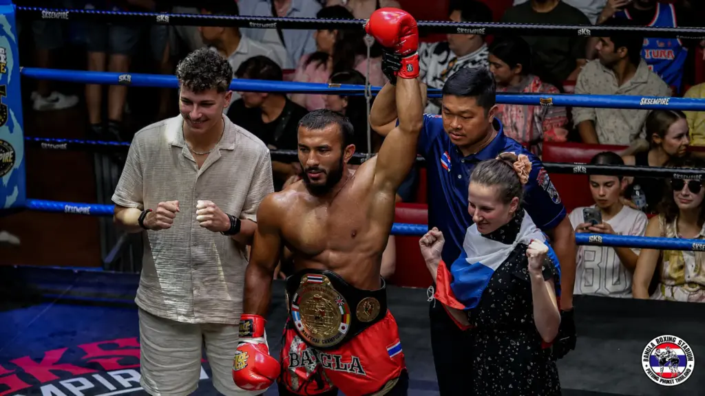 Muay Thai champion with raised arm and victory belt at Phuket boxing stadium