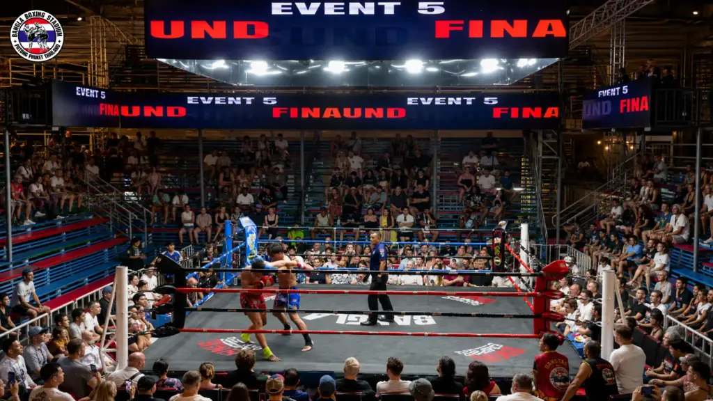 A Phuket Thai boxing match occurring inside a crowded stadium with fighters clashing in the ring.
