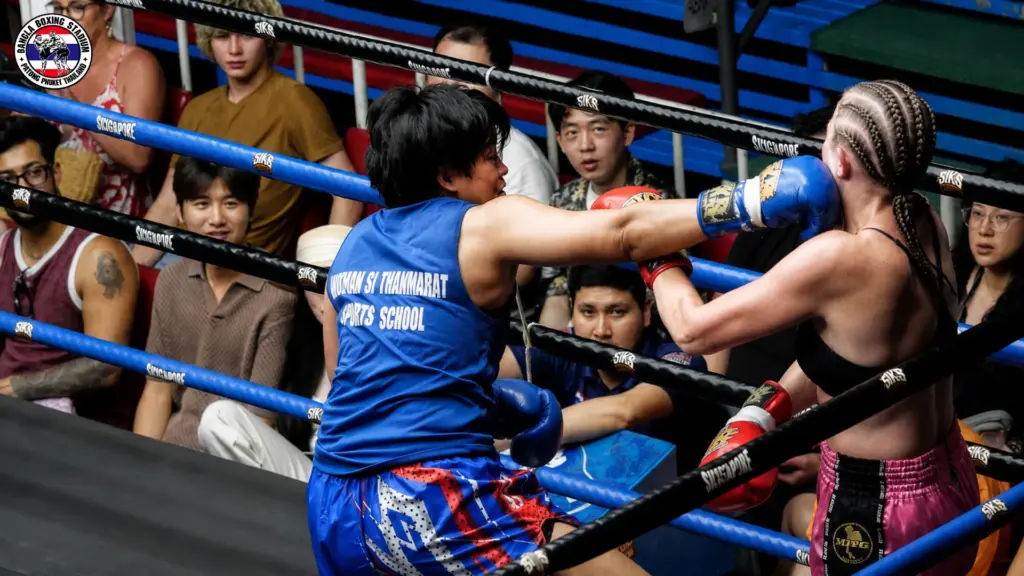 Female athlete wearing a blue jersey lands a punch during a Muay Thai fight in Phuket.