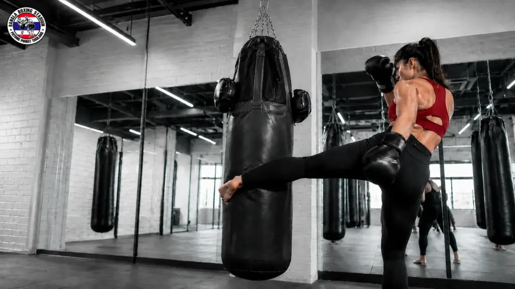 Female athlete practicing high kicks on a heavy bag during Muay Thai training