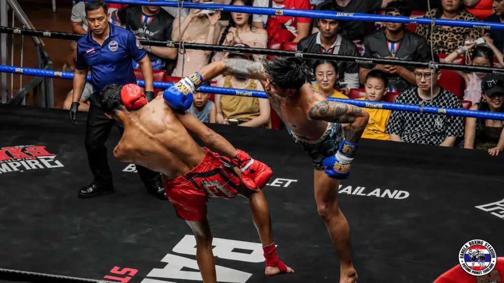 Muay Thai fighters competing in a professional match in a stadium ring with spectators.