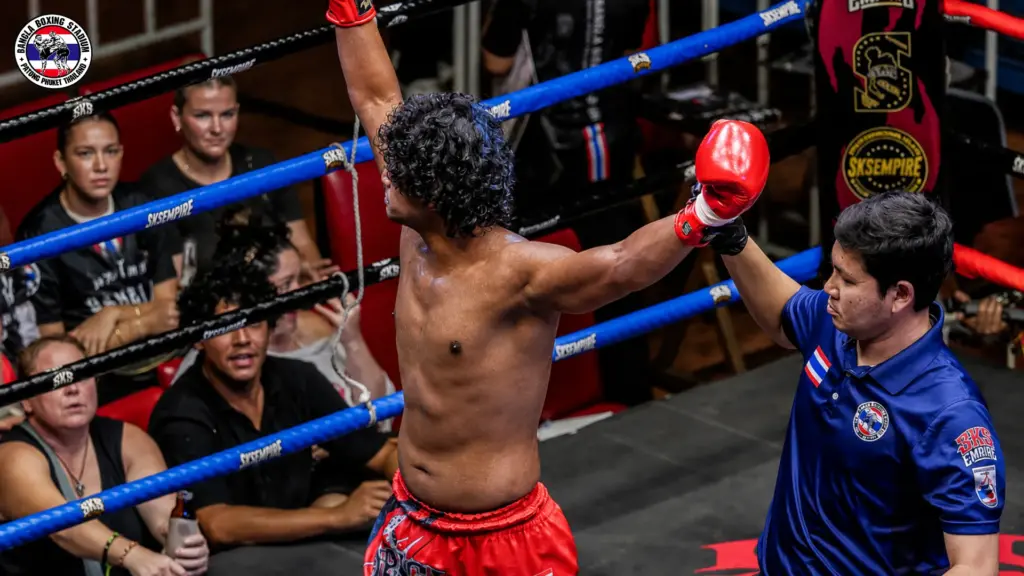 Muay Thai fighter celebrating victory in the ring with a referee during a live show