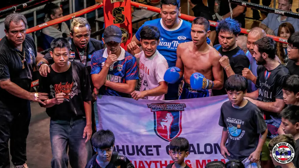 Muay Thai boxer in blue gloves with his coaches and supporters inside the ring