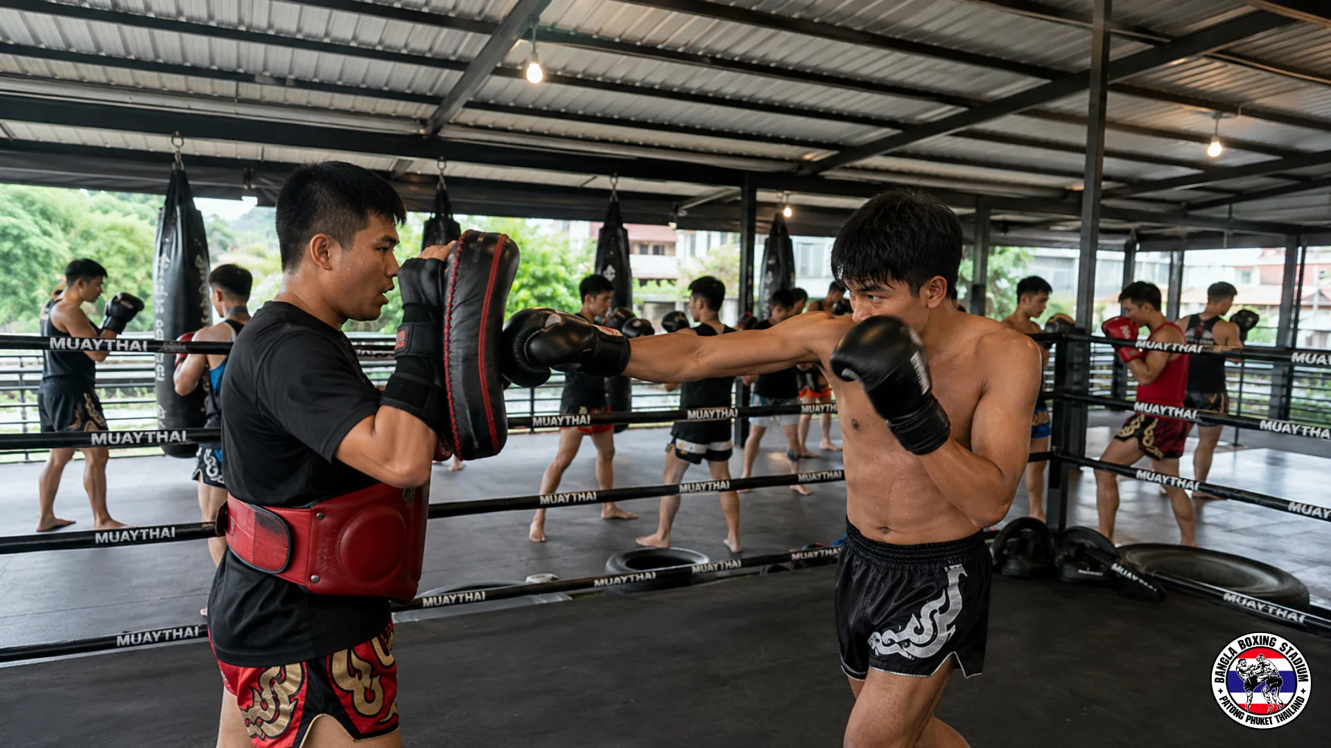 Trainer holding focus mitts for a student in a busy muay thai gym class