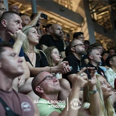 Spectators cheering and filming a Muay Thai fight at Bangla Boxing Stadium