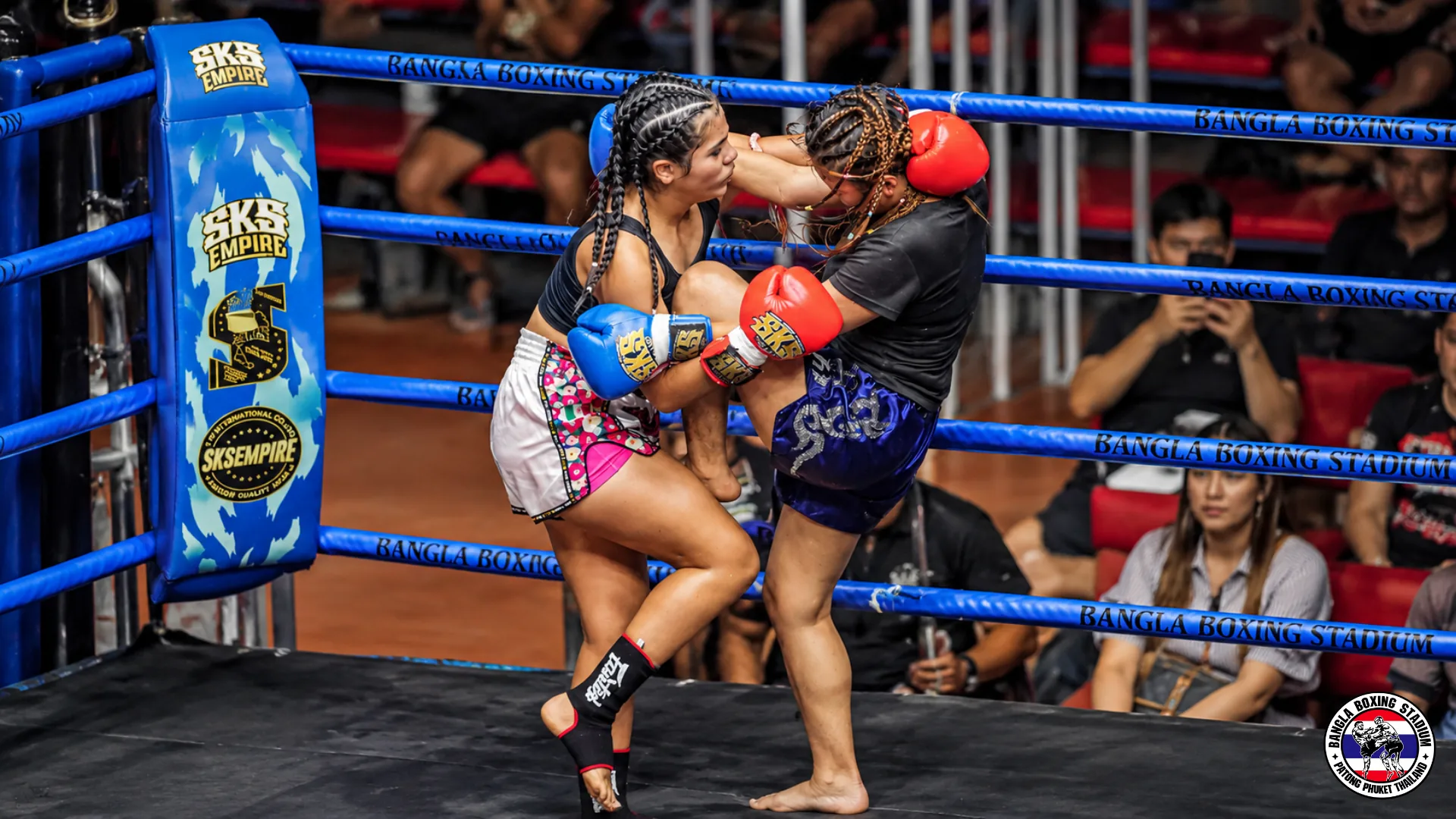 Two Muay Thai fighters locked in a clinch near the blue corner